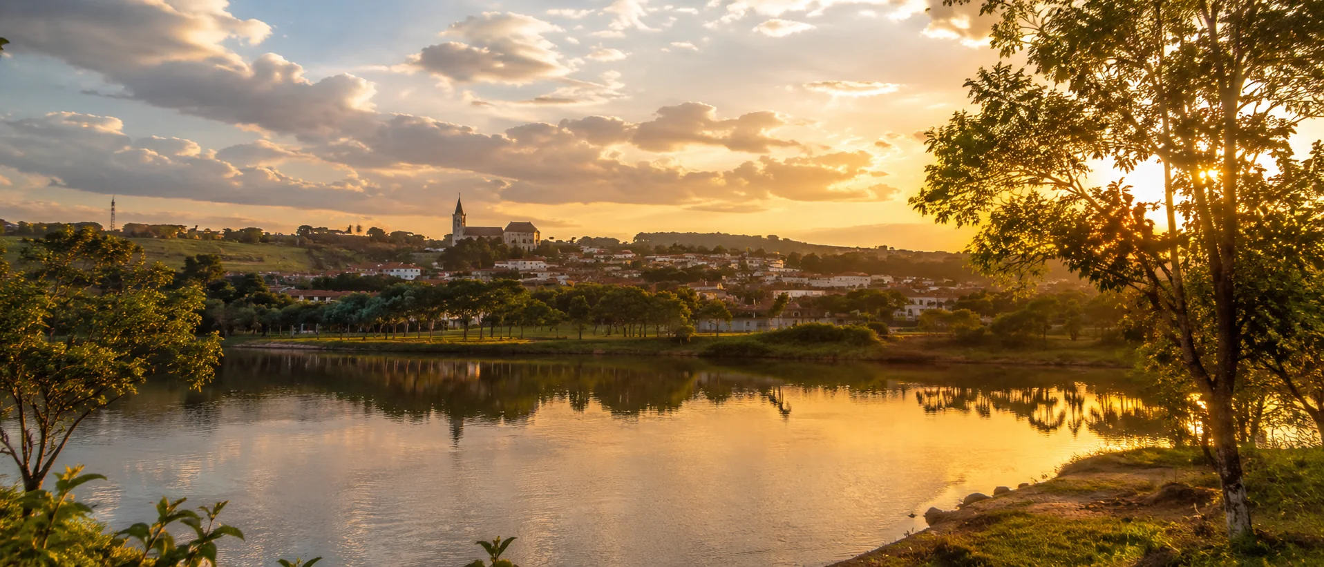 Vista panorâmica de Anicuns ao pôr do sol, com água em primeiro plano e cidade ao fundo