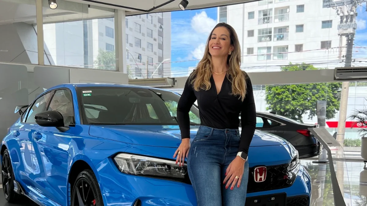Fotografia real de Aline Zia ao lado de automóvel azul em concessionária